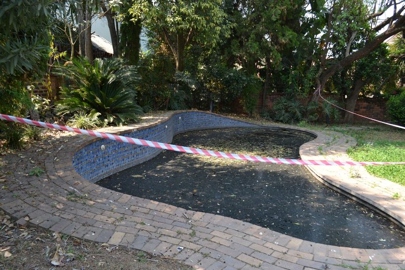 Patricia's pool before work: empty, black standing water, hazard tape across it